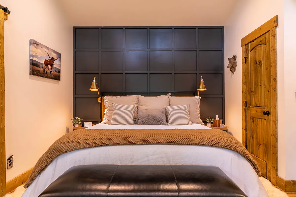 A cozy bedroom scene with a neatly made bed, patterned pillows, a wooden door, and decorative wall art. The linens look plush and inviting, promising restful comfort.